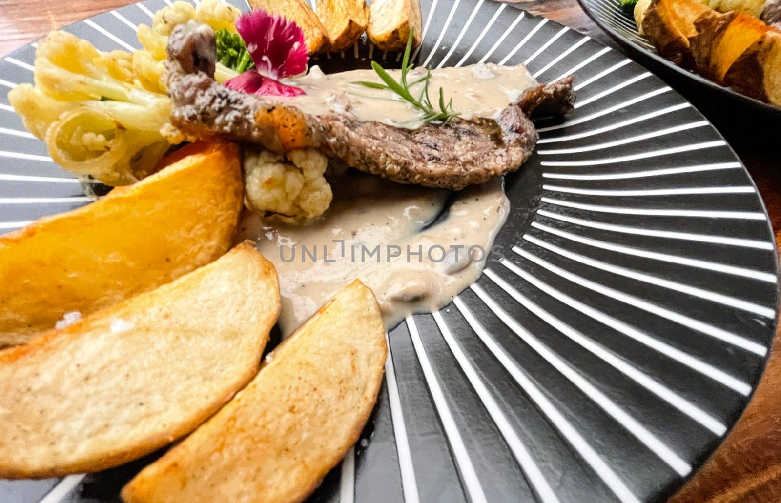 Juicy beef steak with salad and potato wedges along with pepper corn sauce served on black and white stripe on a wooden stone table. Top view