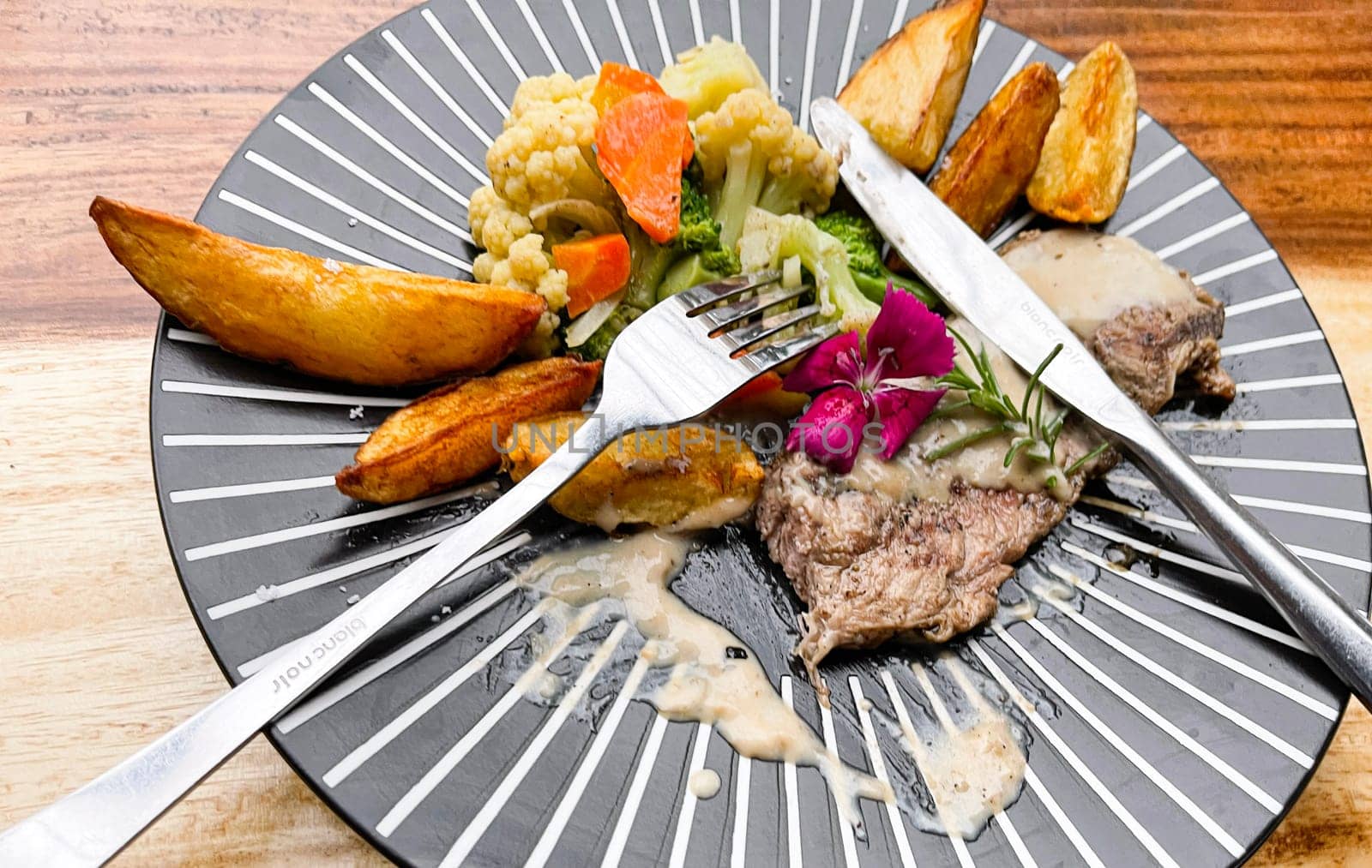 Juicy beef steak with salad and potato wedges along with pepper corn sauce served on black and white stripe on a wooden stone table. Top view