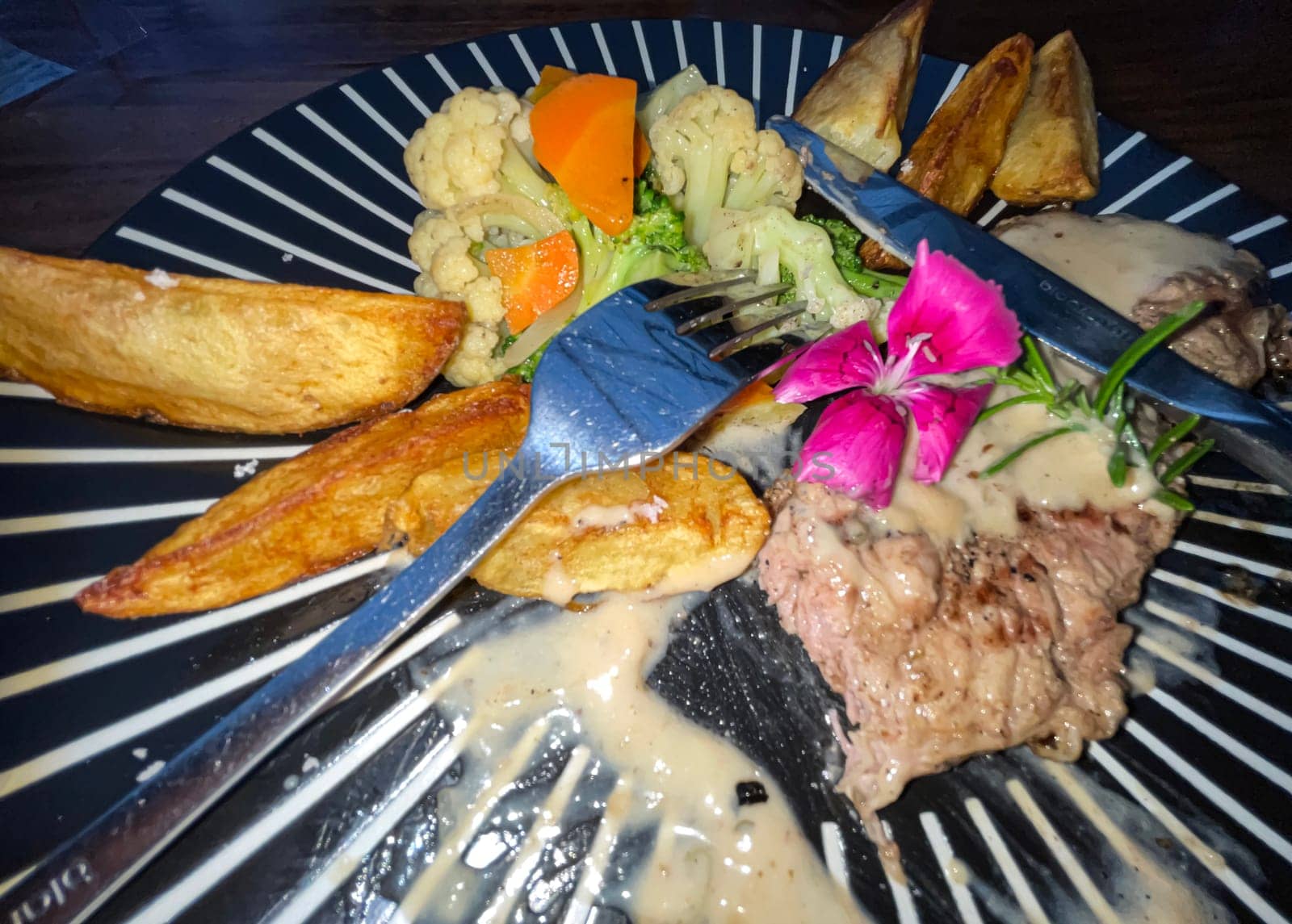 Juicy beef steak with salad and potato wedges along with pepper corn sauce served on black and white stripe on a wooden stone table. Top view