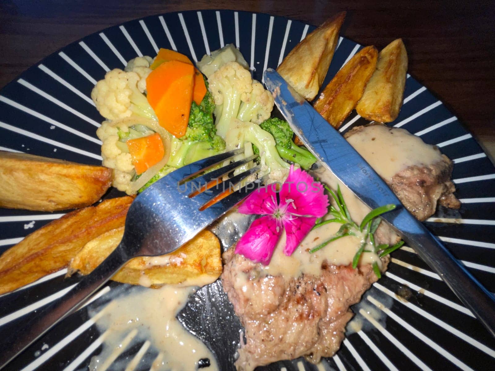 Juicy beef steak with salad and potato wedges along with pepper corn sauce served on black and white stripe on a wooden stone table. Top view