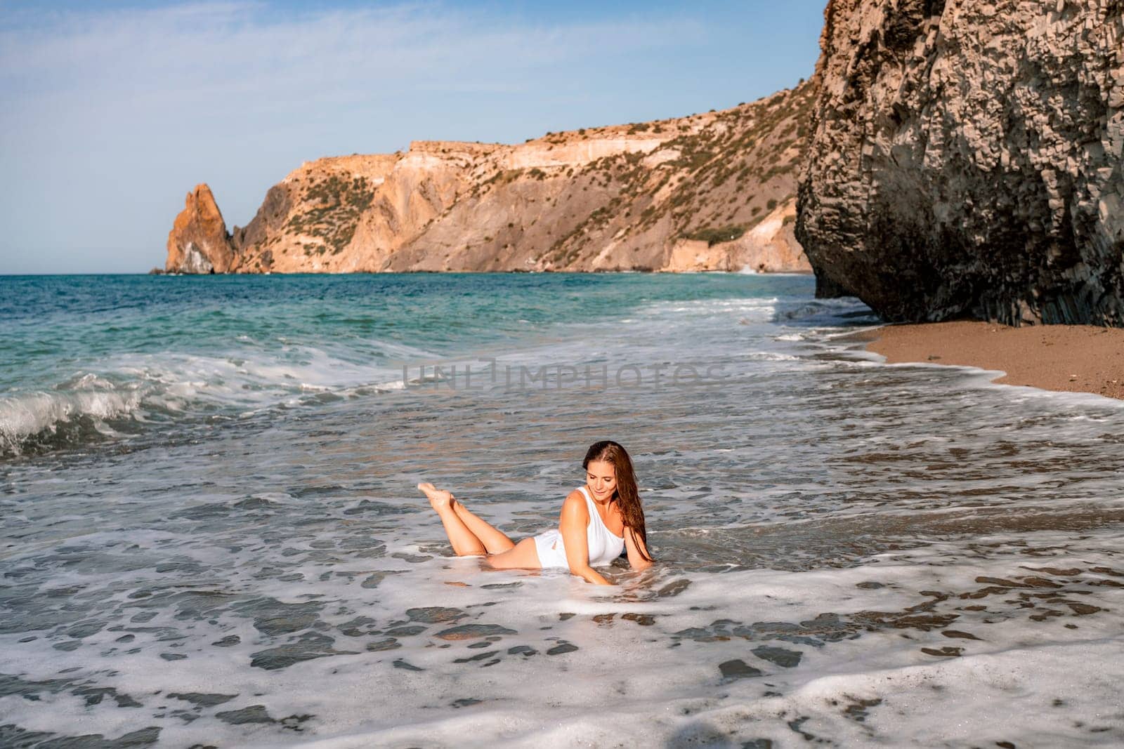 Happy woman in bikini lying on the sea beach. Tanned girl sunbathing on a beautiful shore. Summer vacation or holiday travel concept.