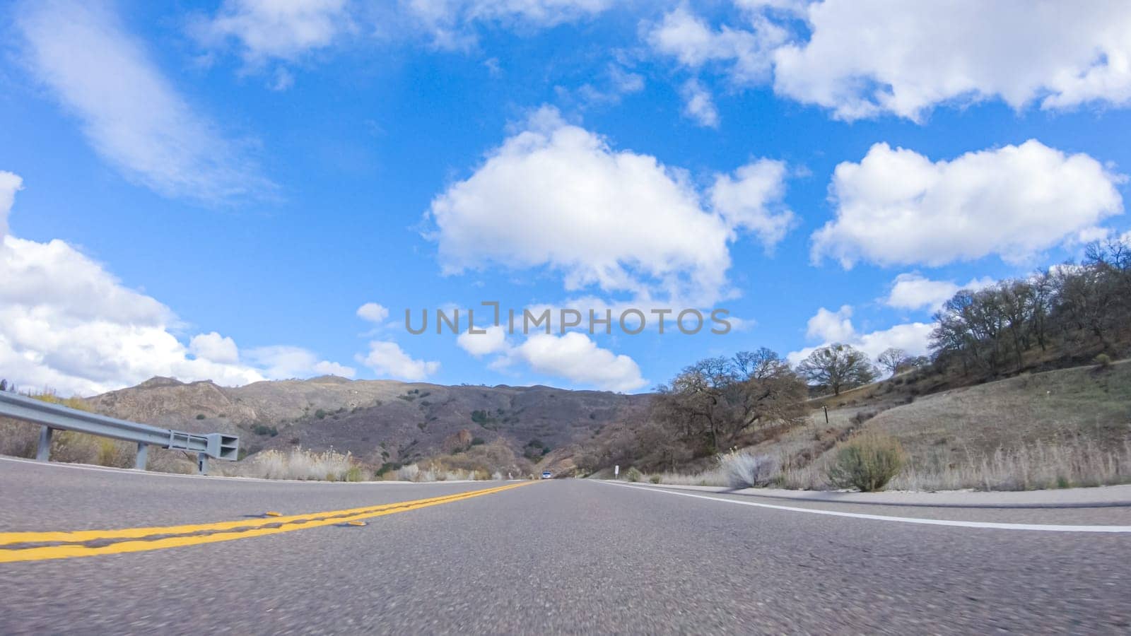 Vehicle is cruising along the Cuyama Highway under the bright sun. The surrounding landscape is illuminated by the radiant sunshine, creating a picturesque and inviting scene as the car travels through this captivating area.