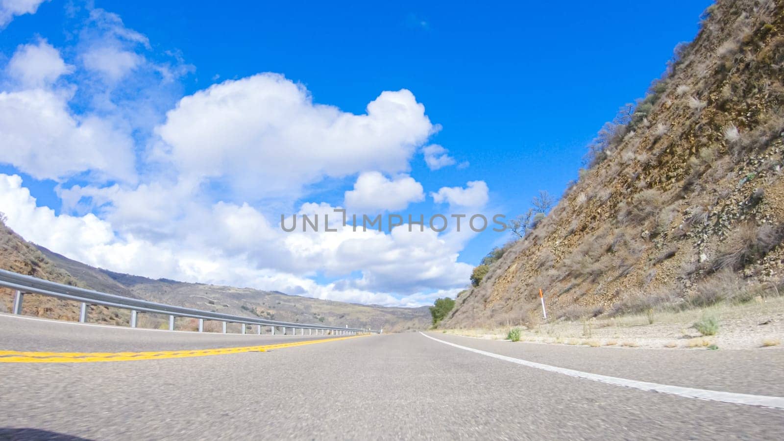 Vehicle is cruising along the Cuyama Highway under the bright sun. The surrounding landscape is illuminated by the radiant sunshine, creating a picturesque and inviting scene as the car travels through this captivating area.