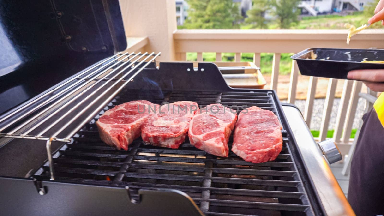 The outdoor two-burner gas grill is put to good use, sizzling with the sound and aroma of ribeye steaks and onion rings being perfectly cooked.