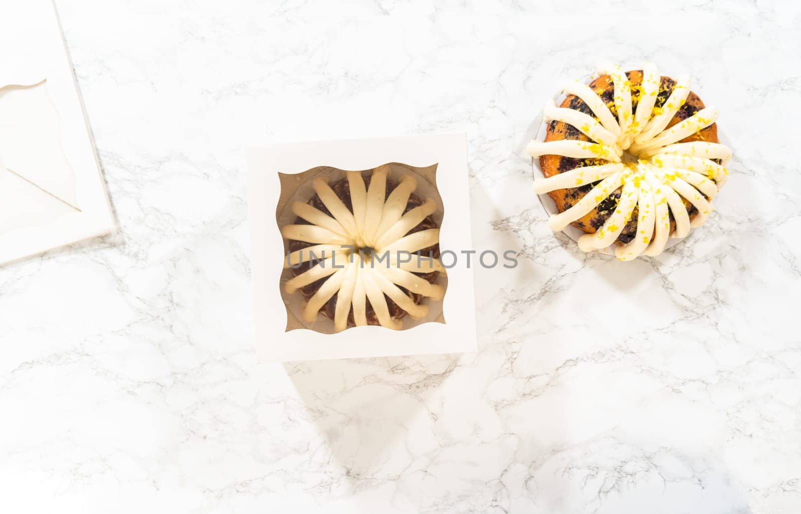 Flat lay. The freshly baked bundt cakes are carefully nestled into white paper boxes, preparing them for secure transportation while maintaining their delectable appearance.