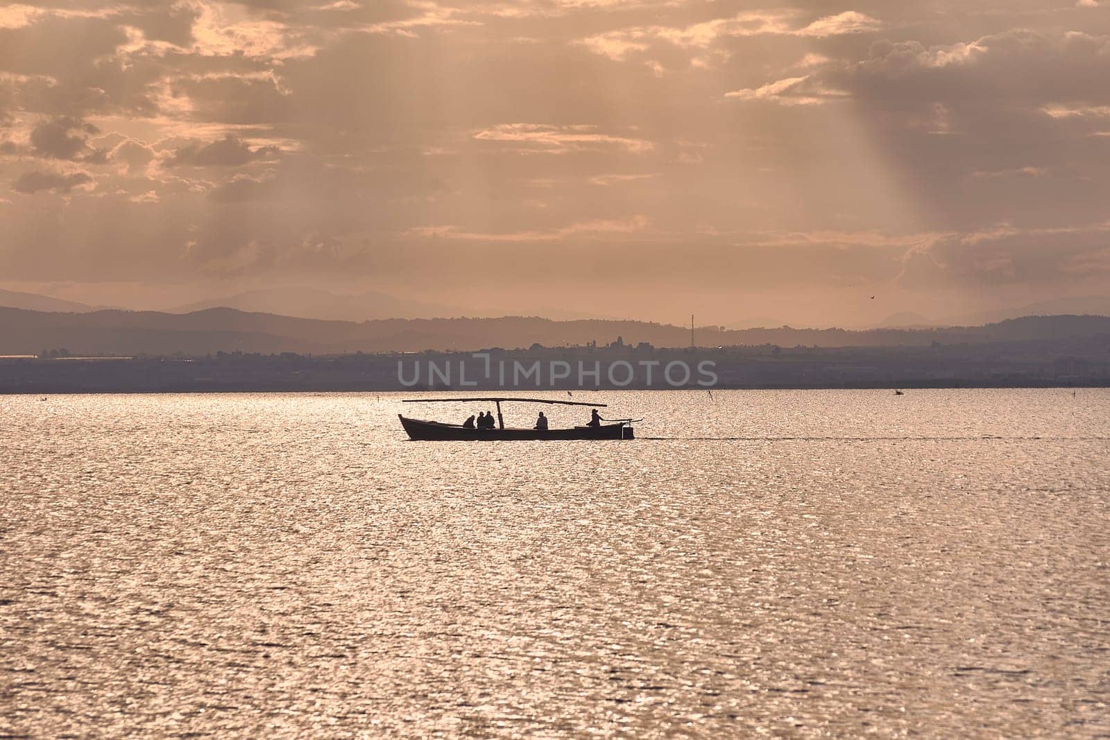 Silhouette of a boat full of people in the Albufera of Valencia. Sunset, sun, calm waters, tradition of reeds.