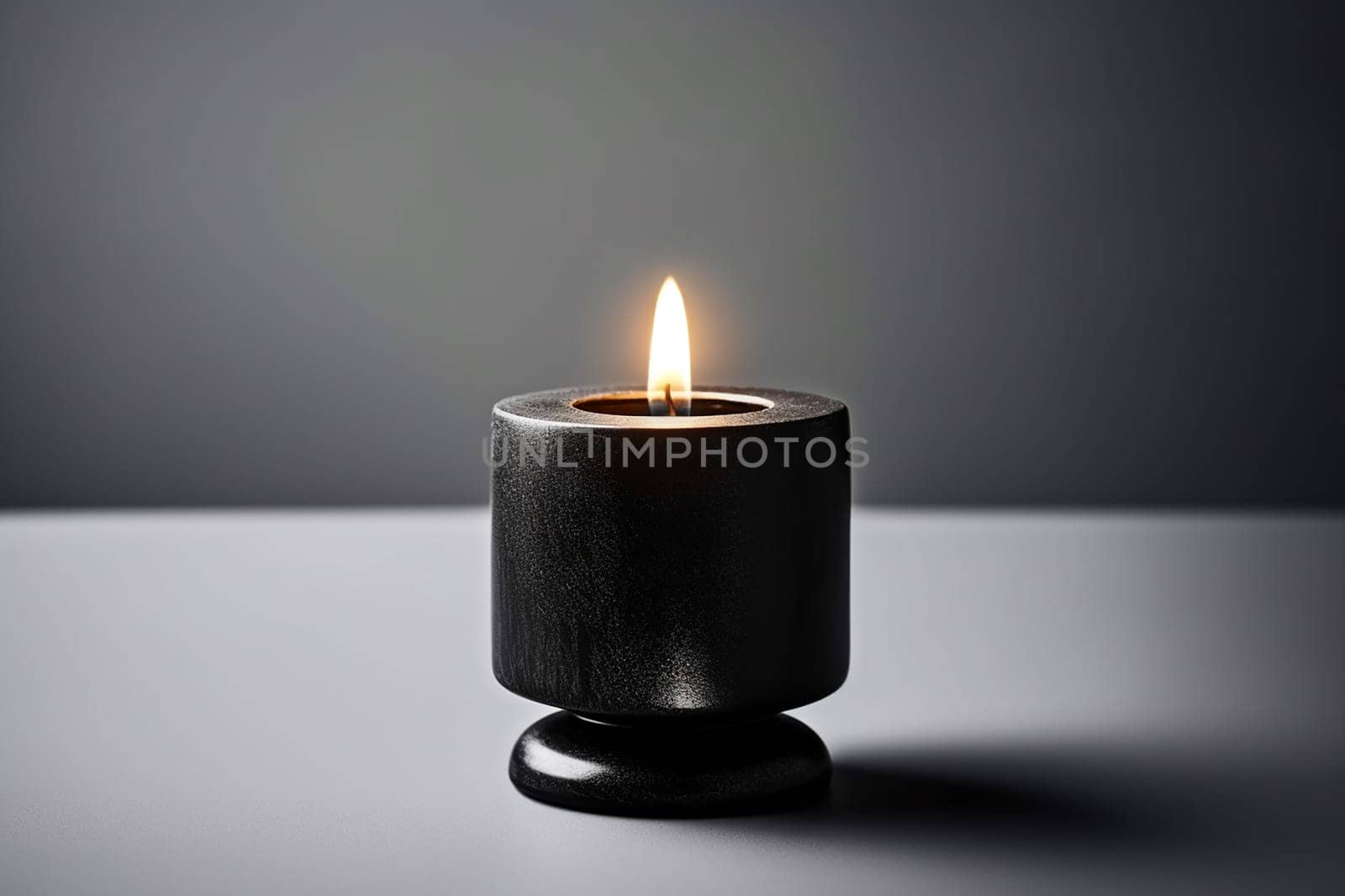 A single lit candle in a black holder against a grey background.