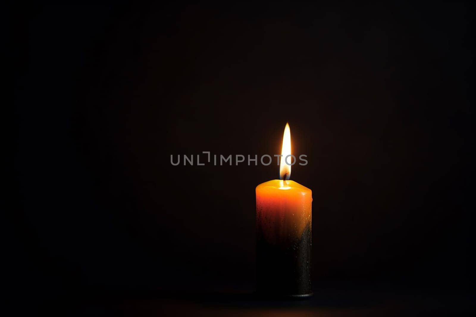 A lone lit candle against a dark background.
