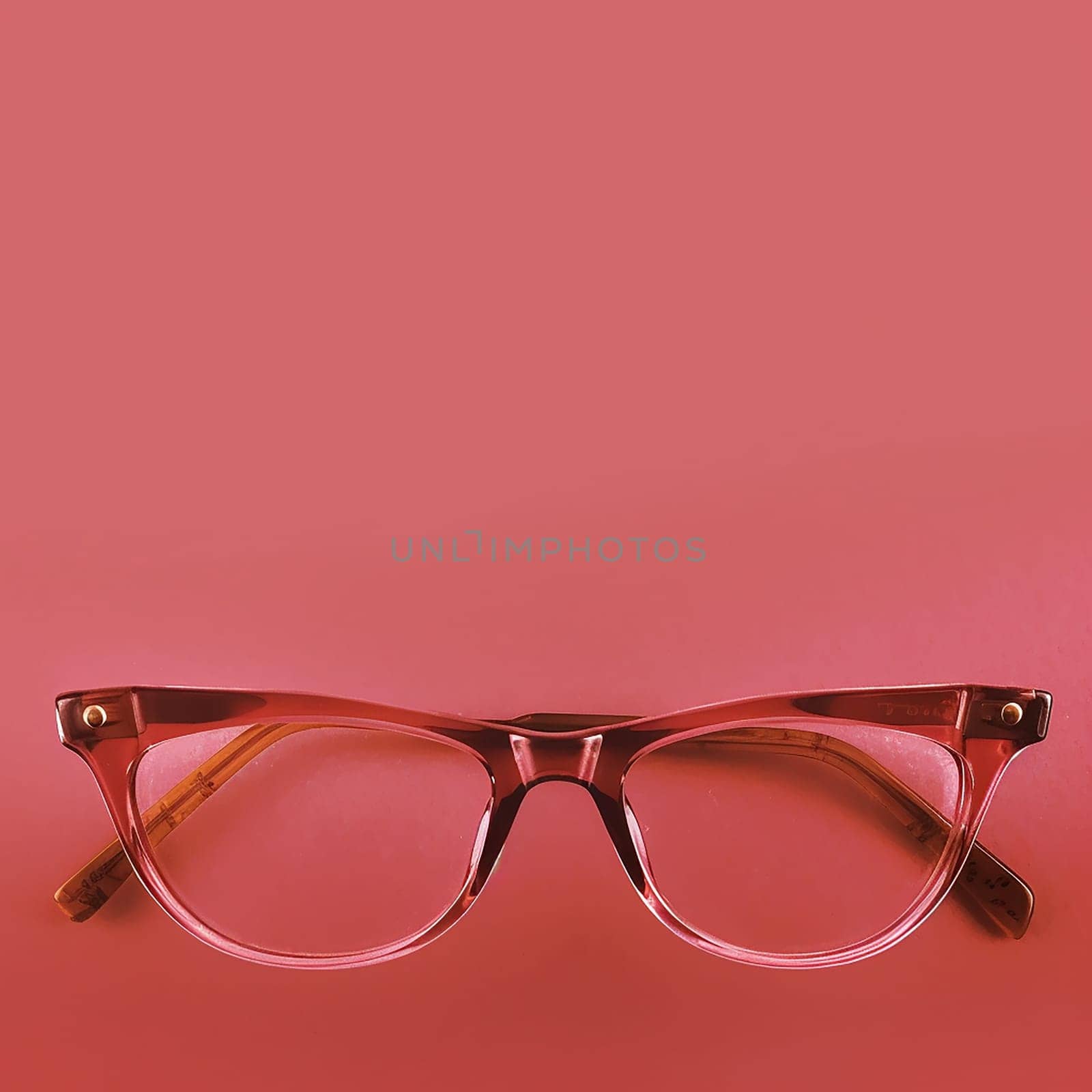 Transparent pink glasses on a plain red background.