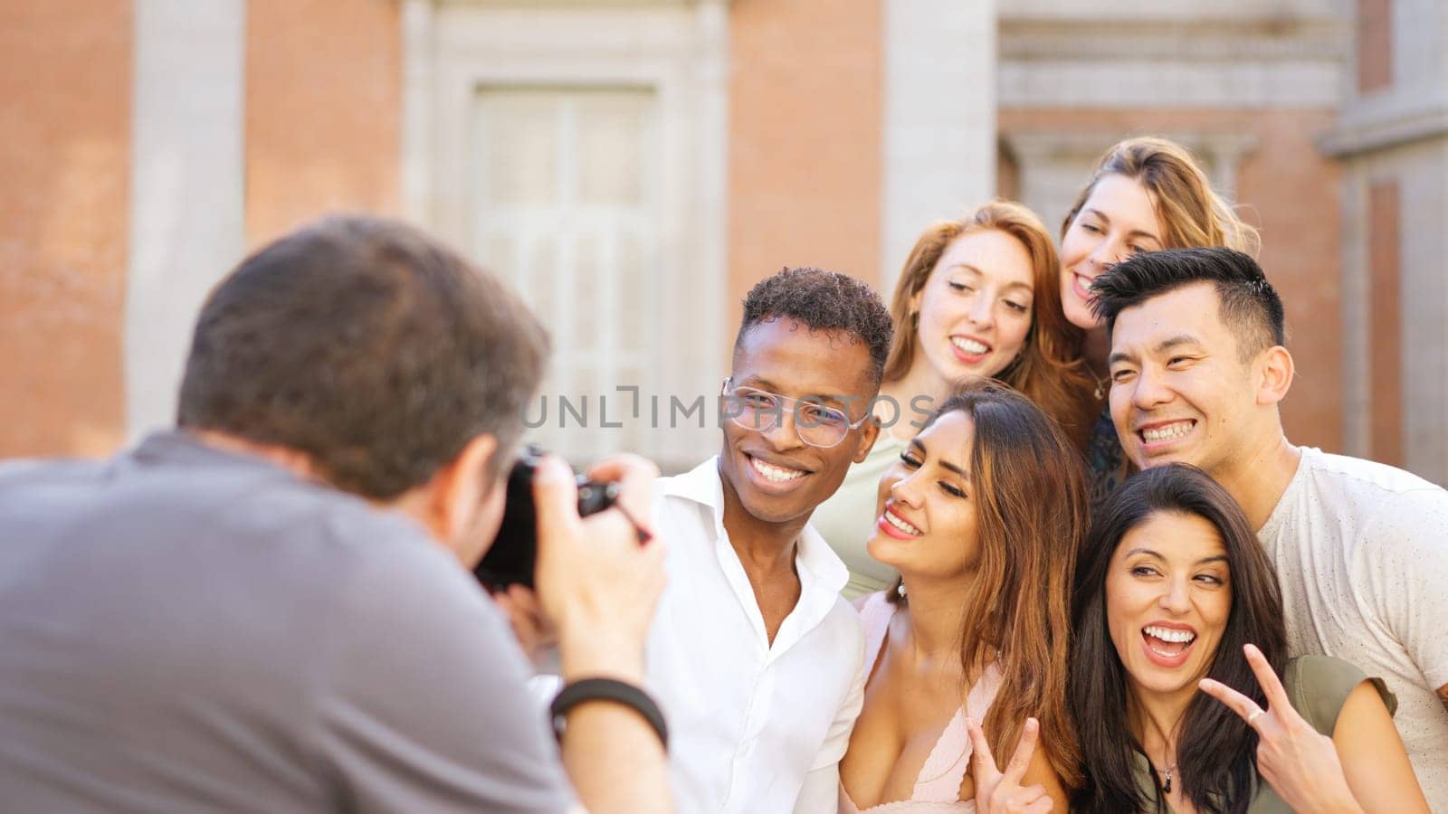 Male photographer taking a photo of a multiracial group of friends in the street