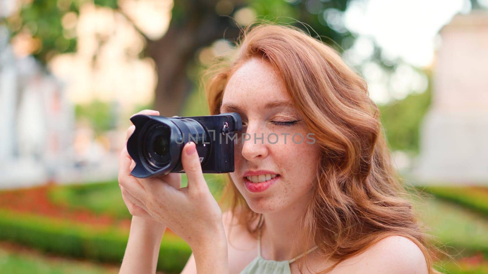 Close up view of a red-haired caucasian woman taking a photo in the street next to a park
