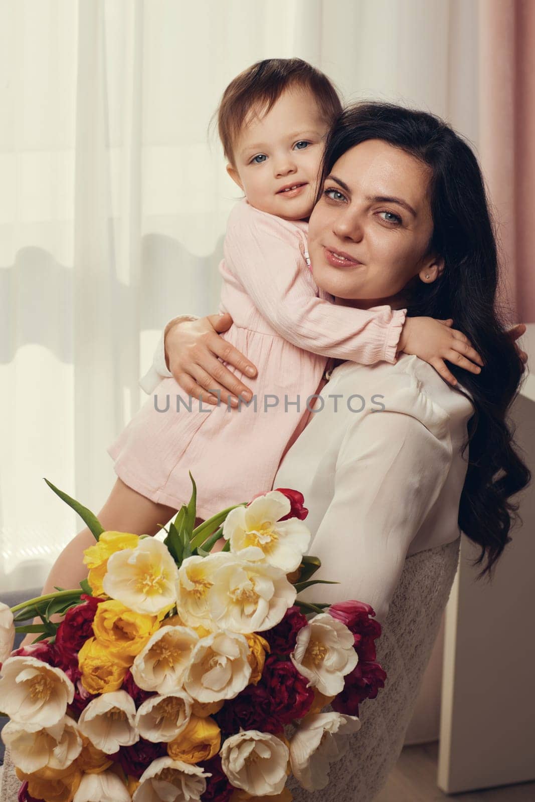 Cute little baby daughter and mom with flowers tulips. Mother and child hugging. Happy mother's day.