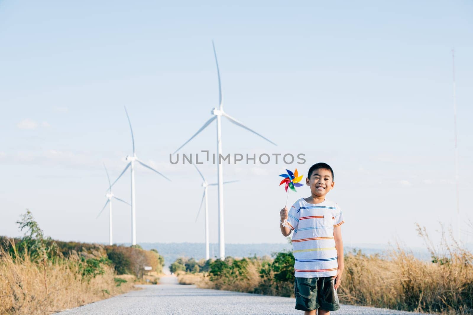 Boy's playful fascination near wind turbines holding a pinwheel toy highlights joy of wind energy by Sorapop