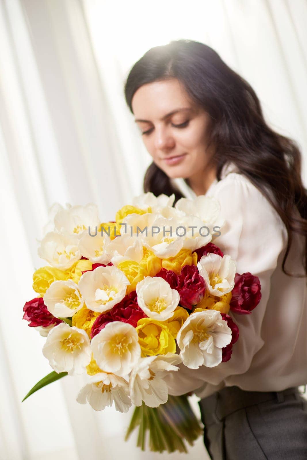 Beautiful woman in the white shirt with spring flowers tulips in hands. Women's Day. focus on flower