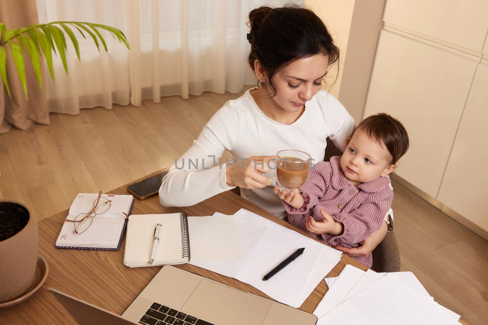 Cheerful pretty businesswoman working at home with her little child girl