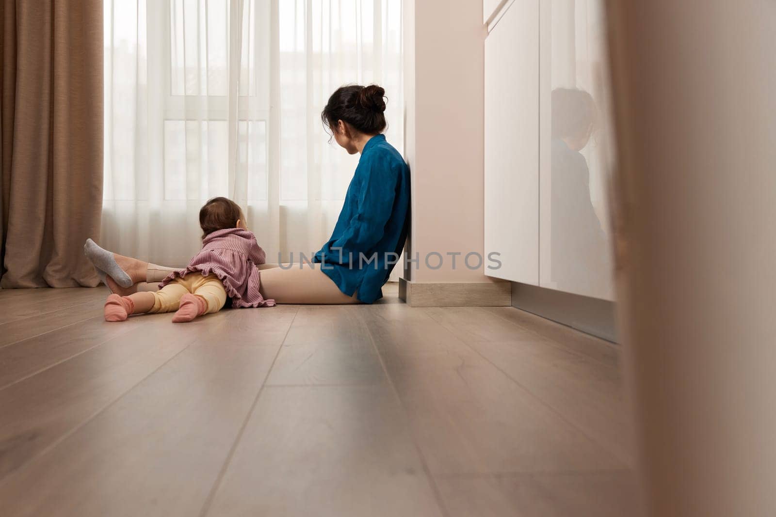 tired woman sitting on the floor with her little child girl at home