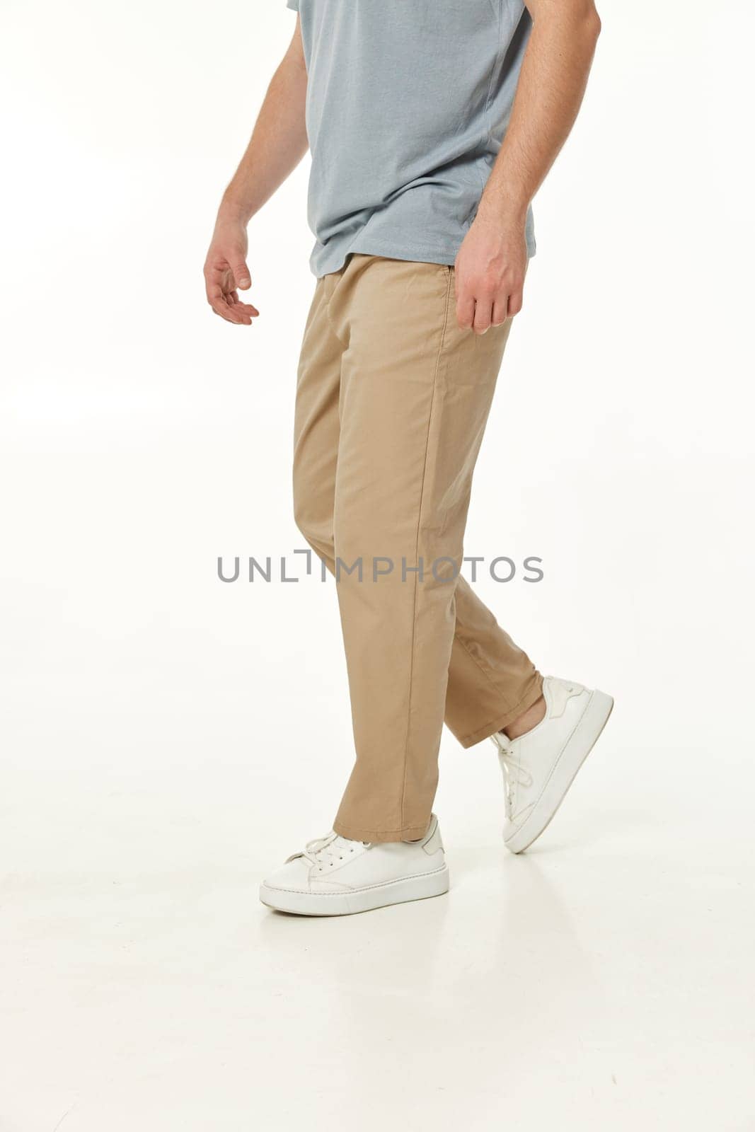 man wearing white sneakers and casual beige pants on studio background. side view