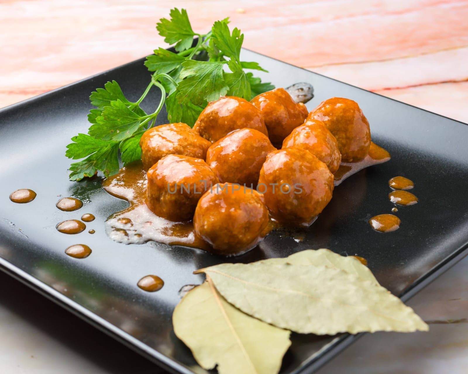 Glazed meatballs garnished with parsley and bay leaf on a black plate, typical food, typical mediterranean mallorcan cuisine typical from balearic islands mallorca, spain,