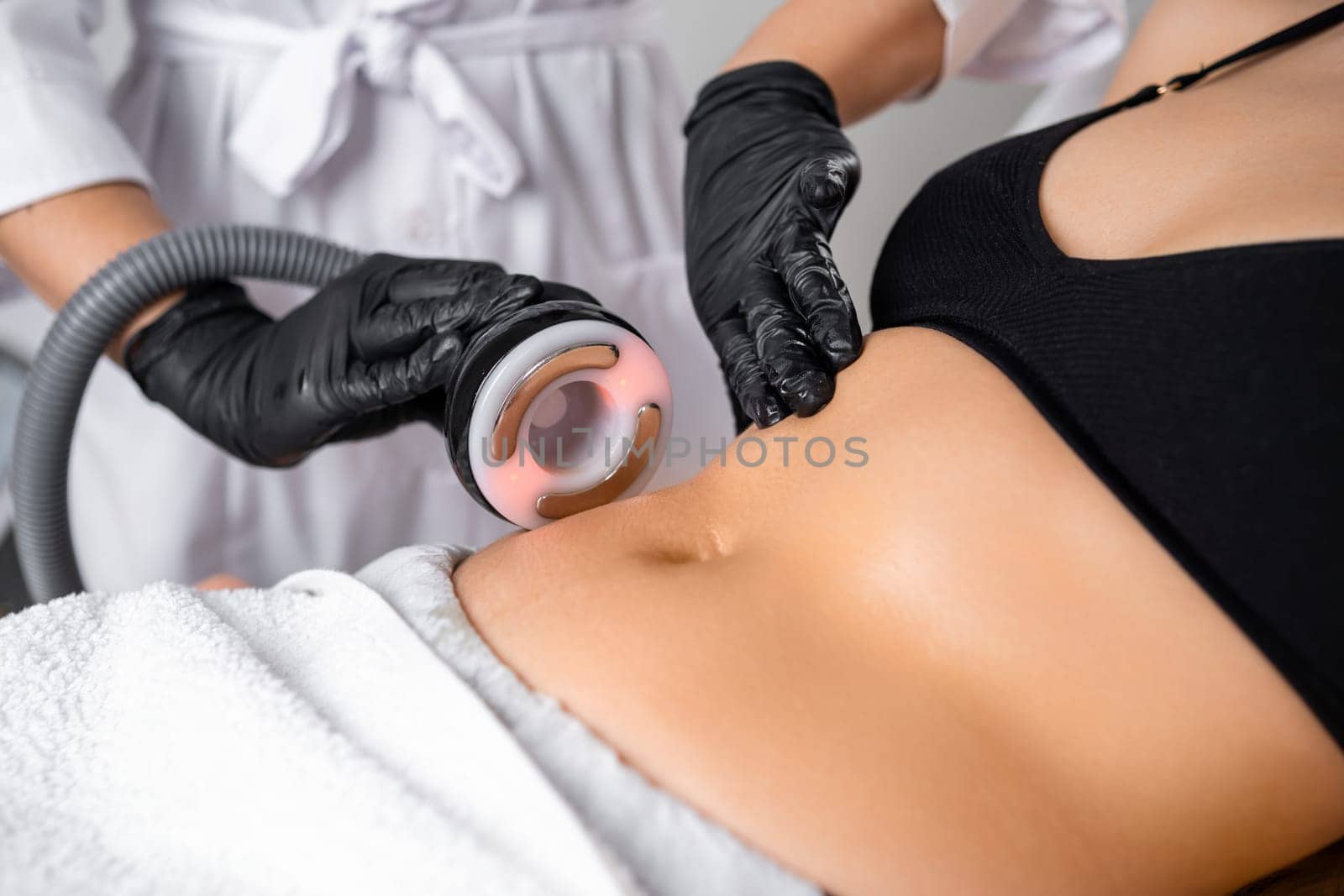 A cosmetologist utilizes an ultrasound device during a lifting procedure on a woman's abdomen. by vladimka