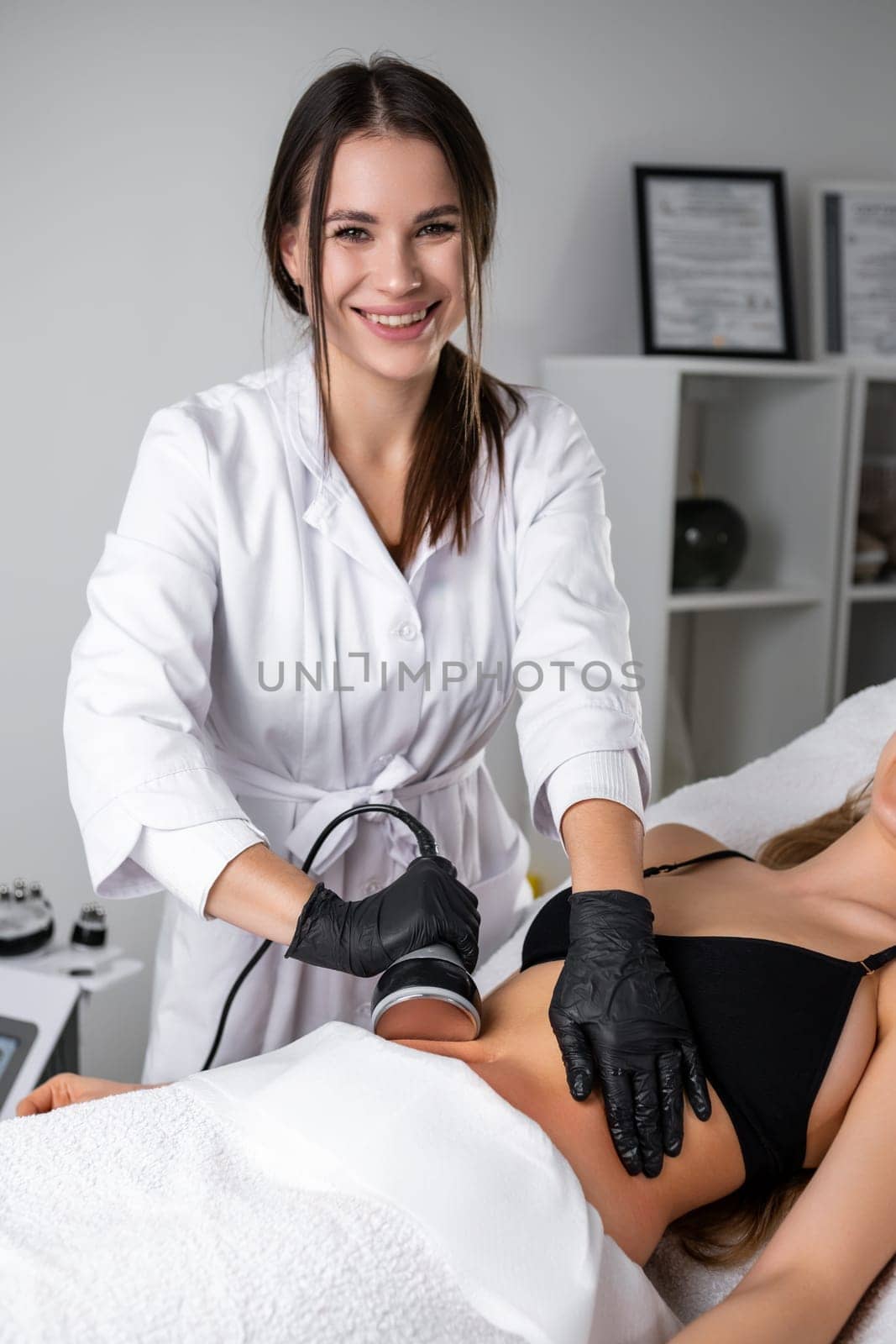 Ultrasound cavitation body contouring treatment for young woman at beauty salon by young beautician.