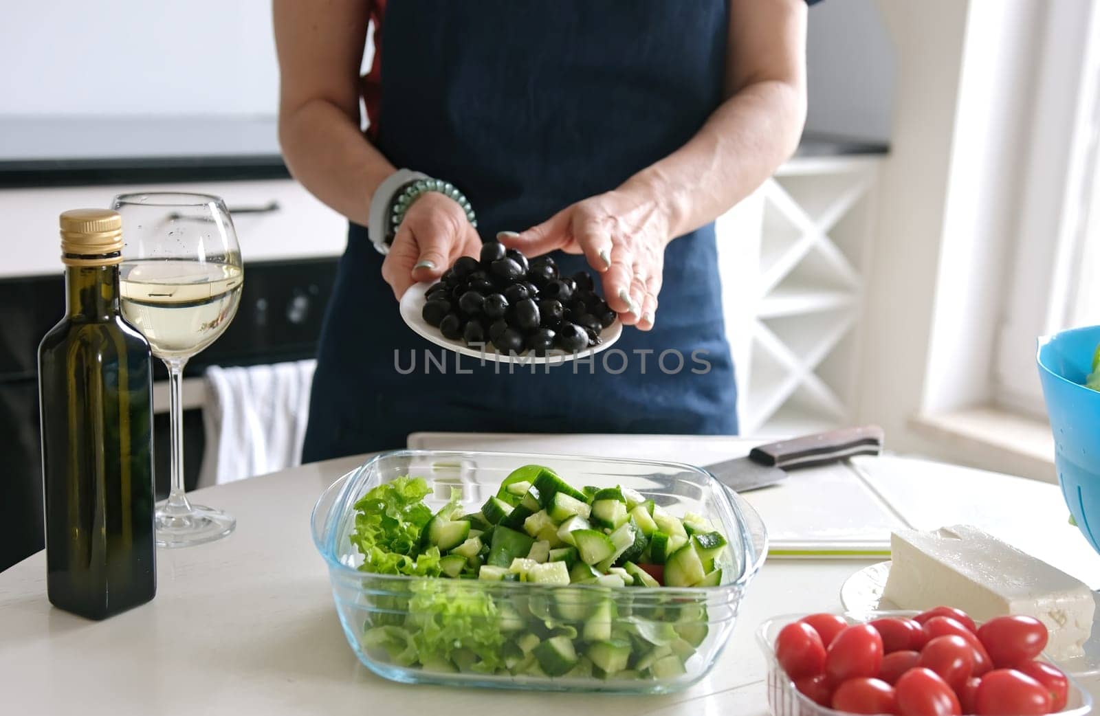 Woman At Home Prepares Greek Salad, Pouring Olives Into Salad Bowl