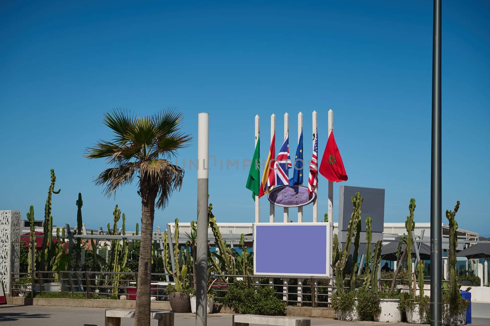 Background with flags of different countries on the promenade. Moroccan, Spanish, European Union, USA and Great Britain flags over blue sky background