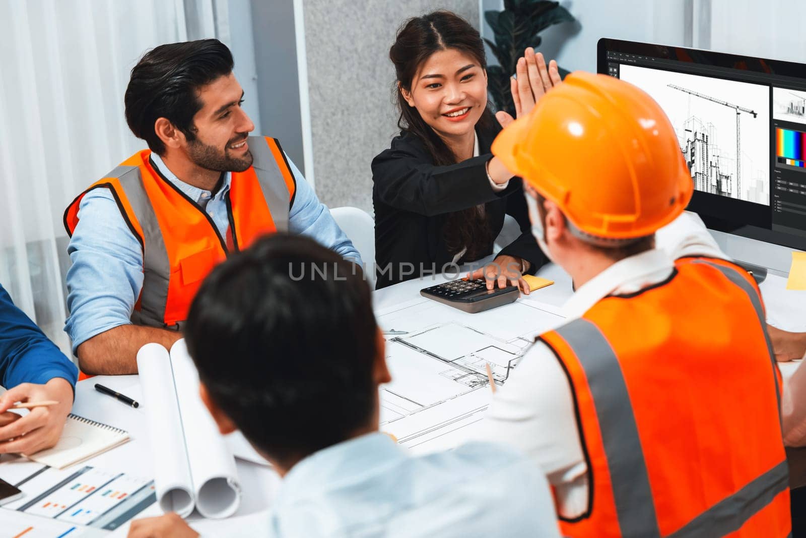 Diverse group of civil engineer and client celebrate and high five after make successful agreement on architectural project, reviewing construction plan and building blueprint at meeting table.Prudent