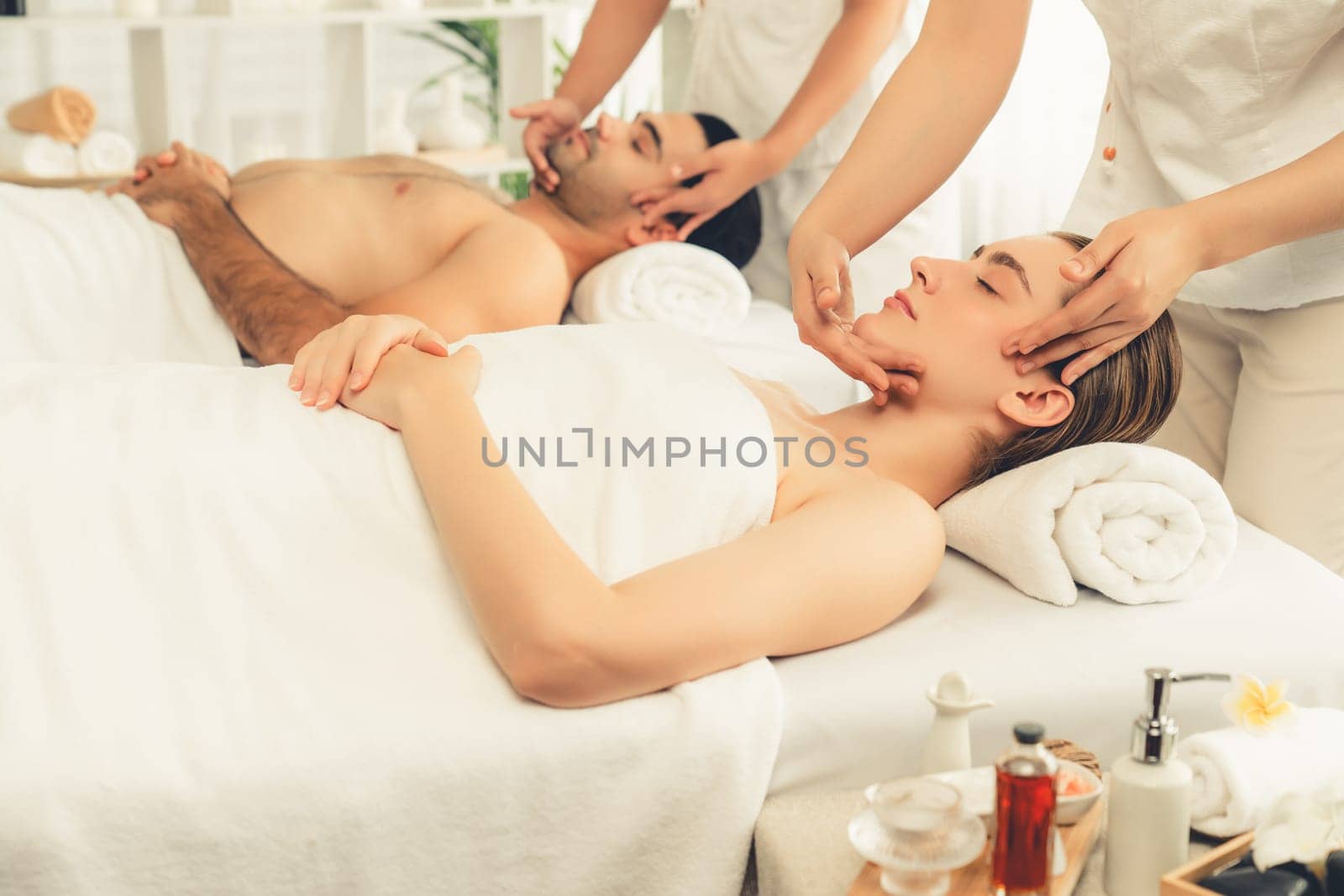 Caucasian couple enjoying relaxing anti-stress head massage and pampering facial beauty skin recreation leisure in dayspa modern light ambient at luxury resort or hotel spa salon. Quiescent