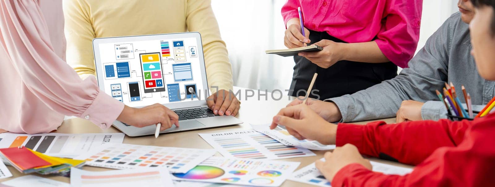 Cropped image of interior designer team presents color by using color swatches while laptop displayed UI and UX designs for mobiles app and website. Creative design and business concept. Variegated.