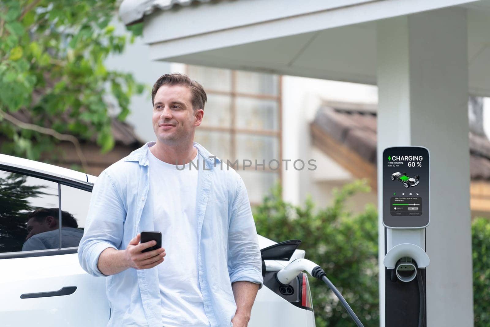 Modern eco-friendly man recharging electric vehicle from home EV charging station. Innovative EV technology utilization for tracking energy usage to optimize battery charging at home. Synchronos