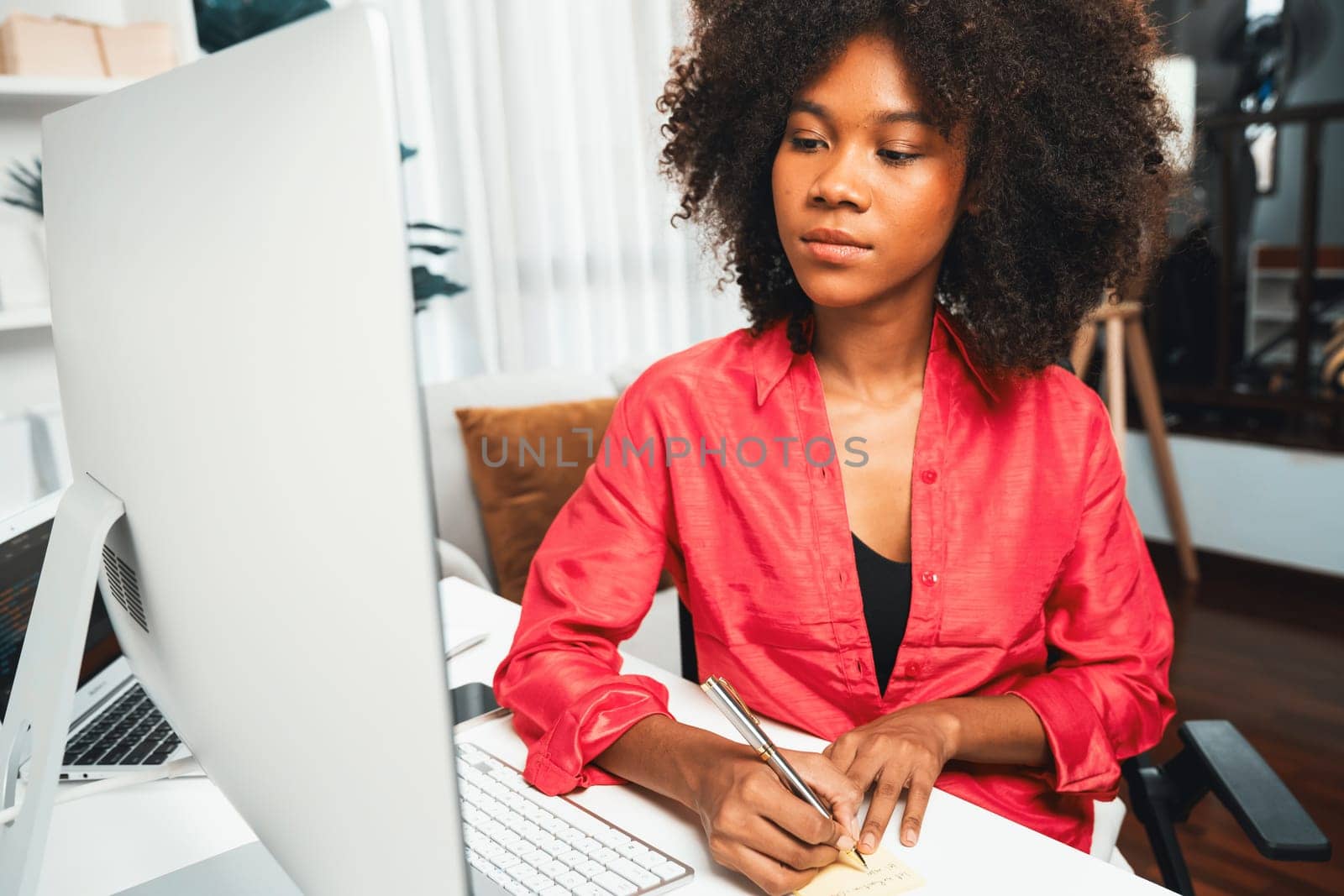 African american businesswoman creating project job's customer on computer with standing on desk at home office, writing crucial information on the paper. Concept of creative working life. Tastemaker.