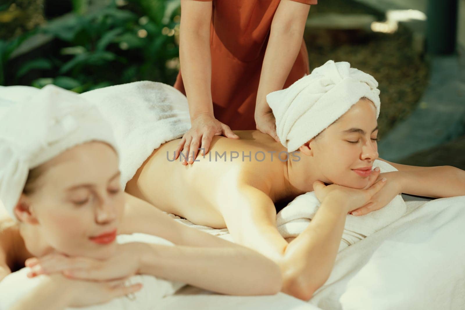 Couple of beautiful young woman lie on white spa bed during having back massage. Attractive caucasian woman having back massage at traditional spa room. Relaxing and healthy concept Tranquility.