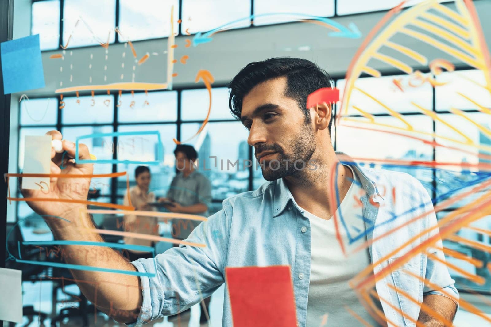 Portrait of young handsome businessman writing marketing idea by using colorful marker on glass wall with graph and mind map. Manager sharing idea or financial strategy. Business plan. Tracery.