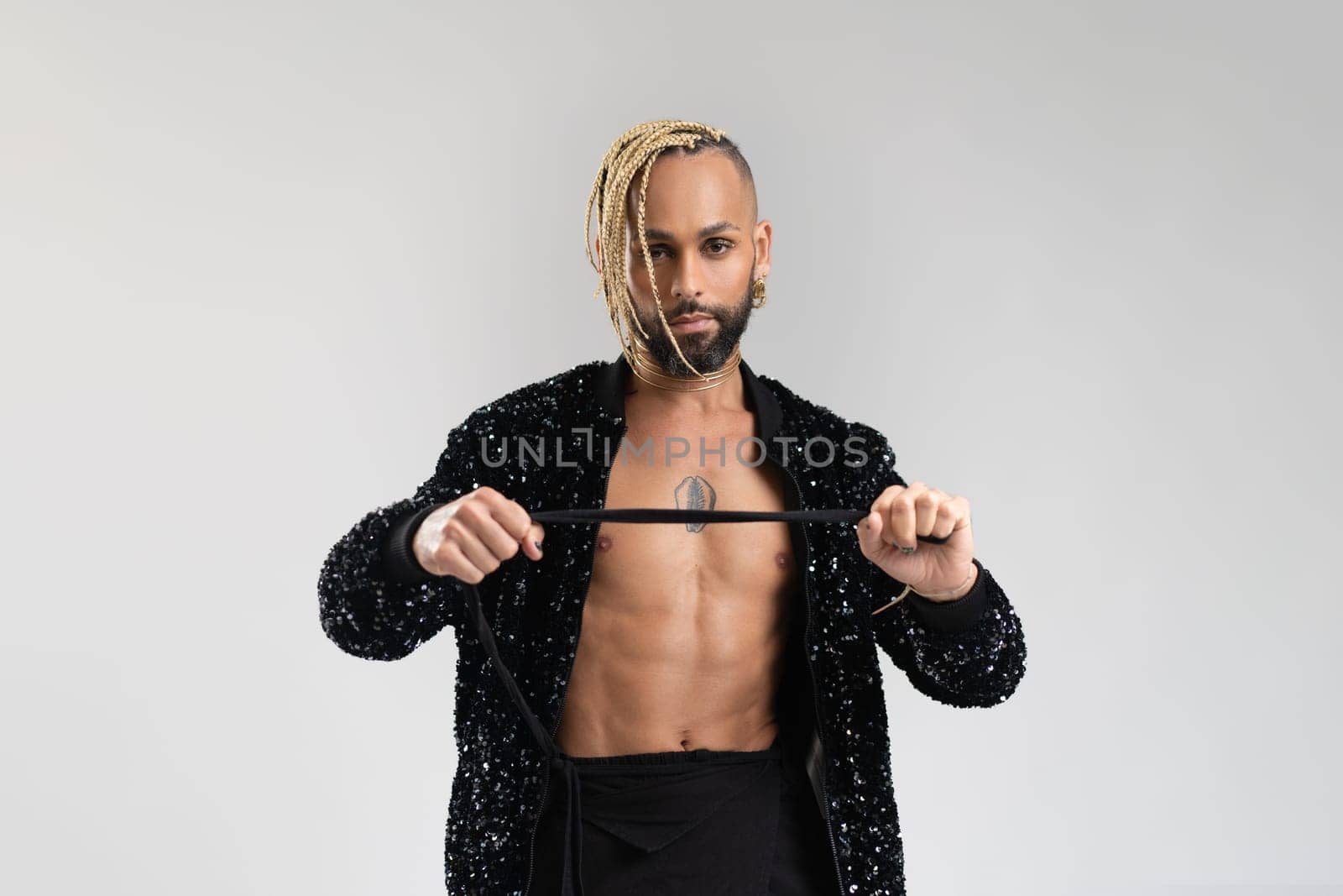 Man wearing stylish jacket with sequins. Afro-american homosexual male posing in photo studio on white background. Bearded gay with beard and make up