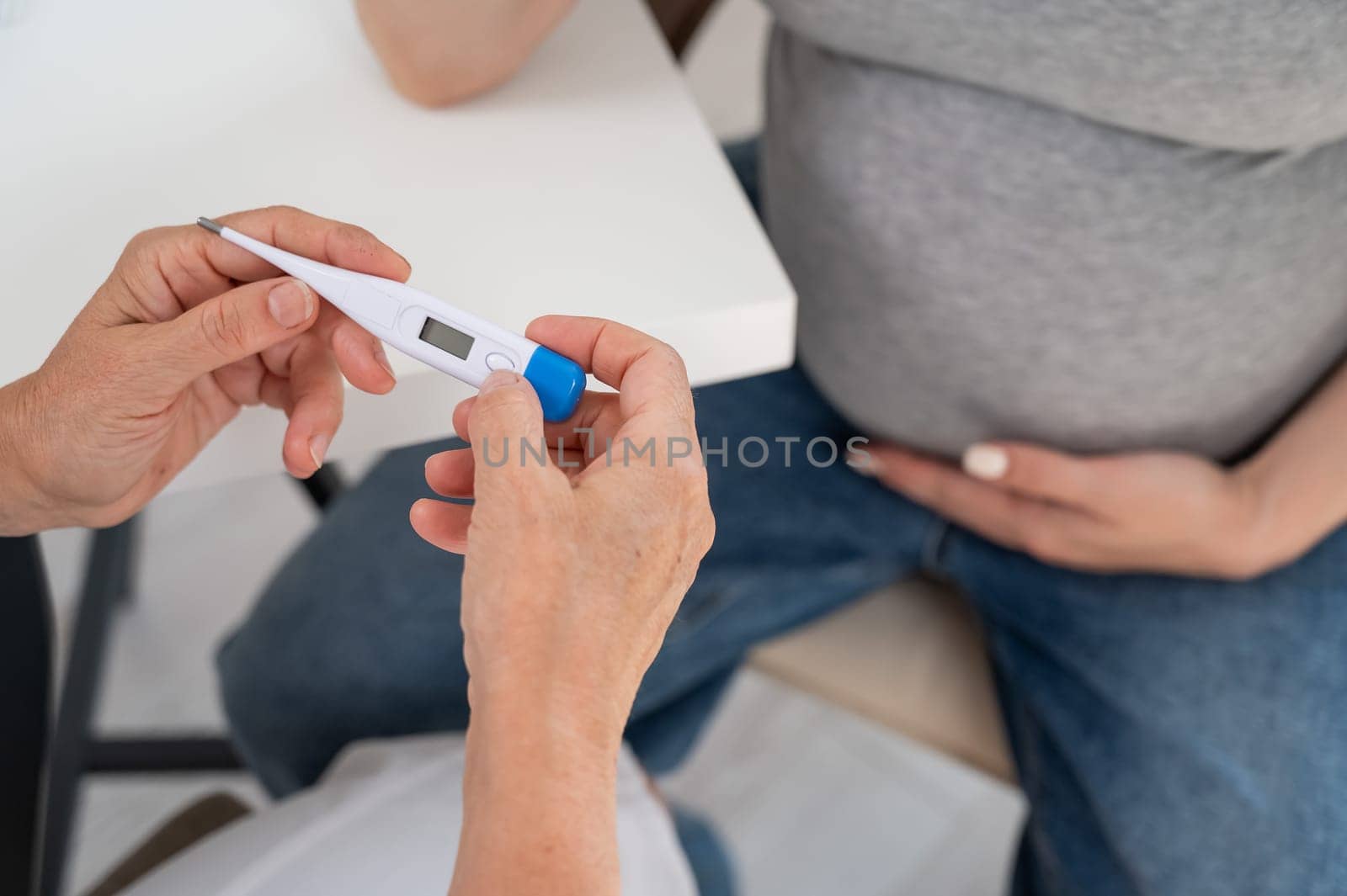 A pregnant woman visits a doctor. Therapist holding an electronic thermometer