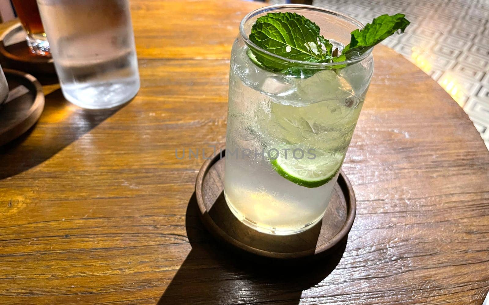 Selective focus, Delicious refreshing summer mojito with ice, lime and mint in a glass with grops. wood background. Copy space. Cold lemonade, tonic.