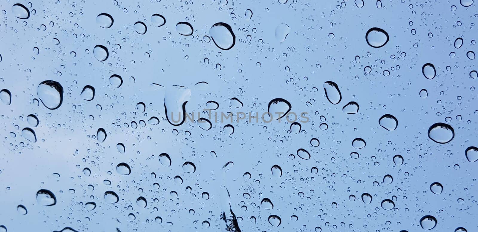 Water droplets perspective through window glass surface against blue sky good for multimedia content backgrounds