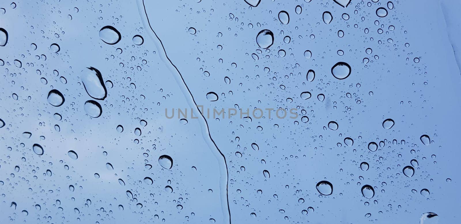 Water droplets perspective through window glass surface against blue sky good for multimedia content backgrounds