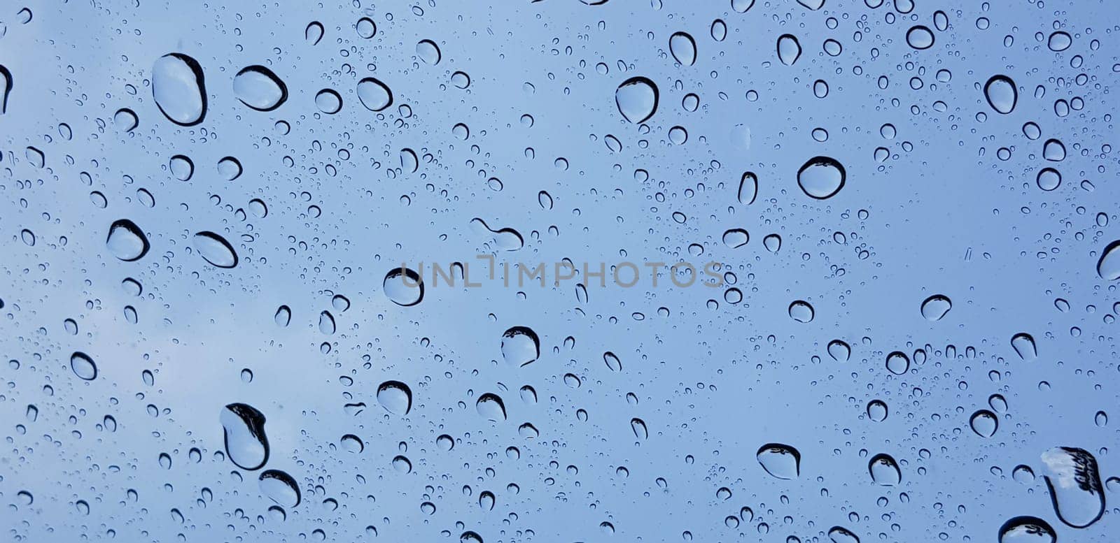 Water droplets perspective through window glass surface against blue sky good for multimedia content backgrounds