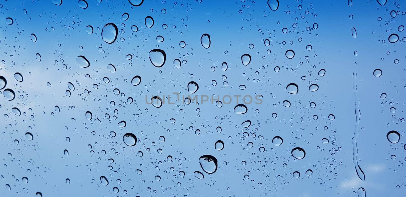 Water droplets perspective through window glass surface against blue sky good for multimedia content backgrounds