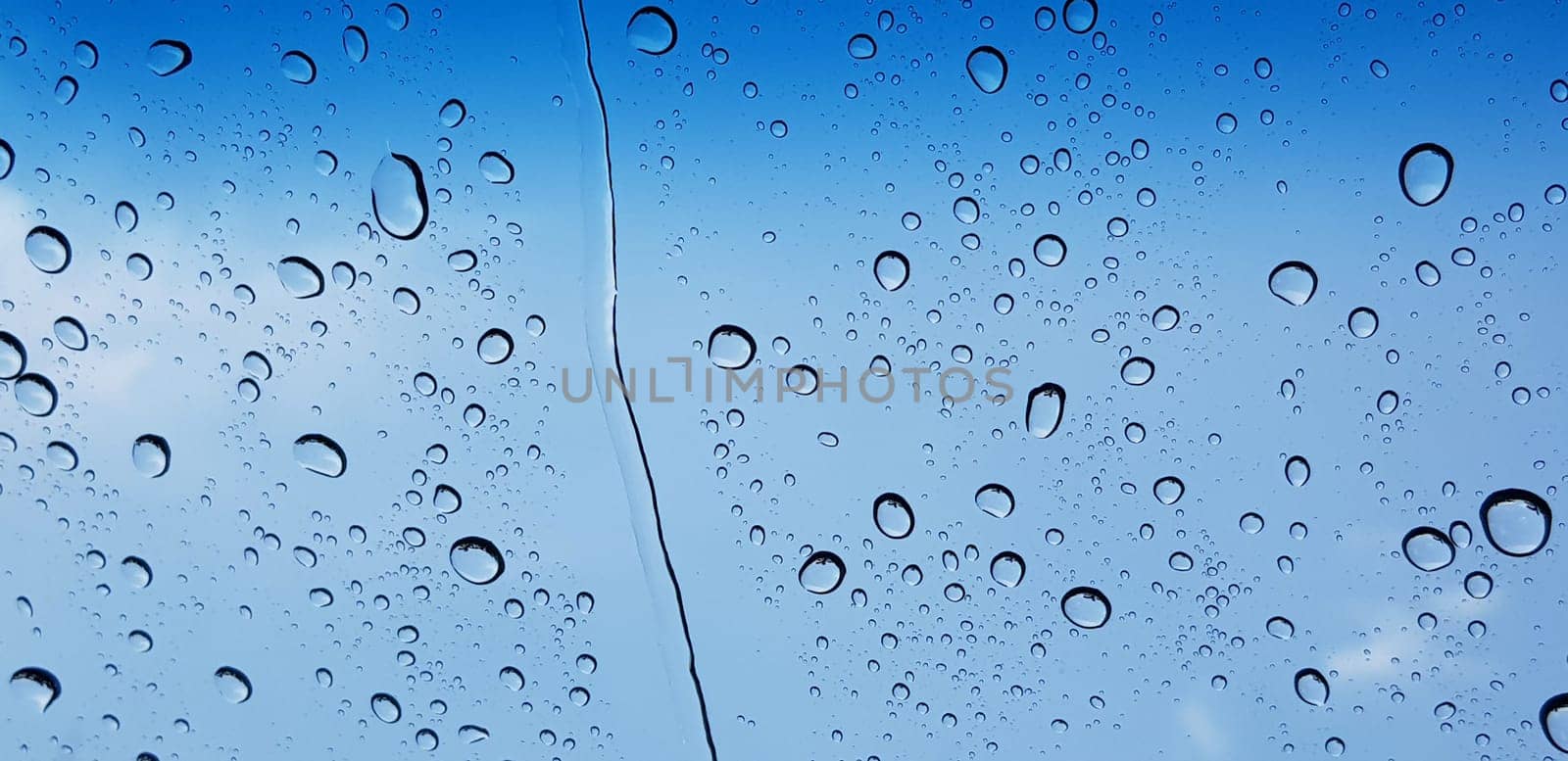 Water droplets perspective through window glass surface against blue sky good for multimedia content by antoksena