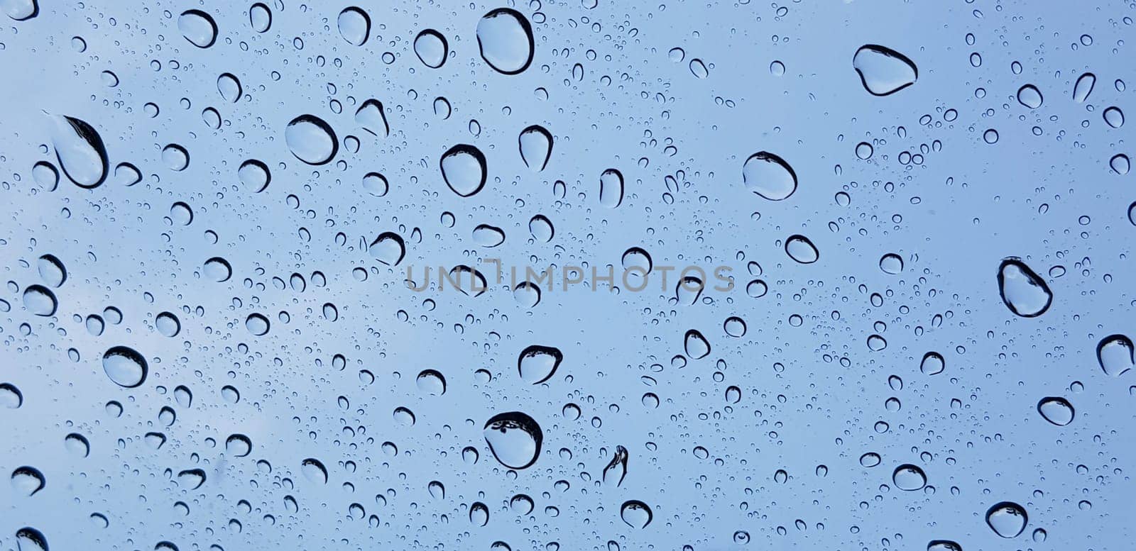 Water droplets perspective through window glass surface against blue sky good for multimedia content backgrounds