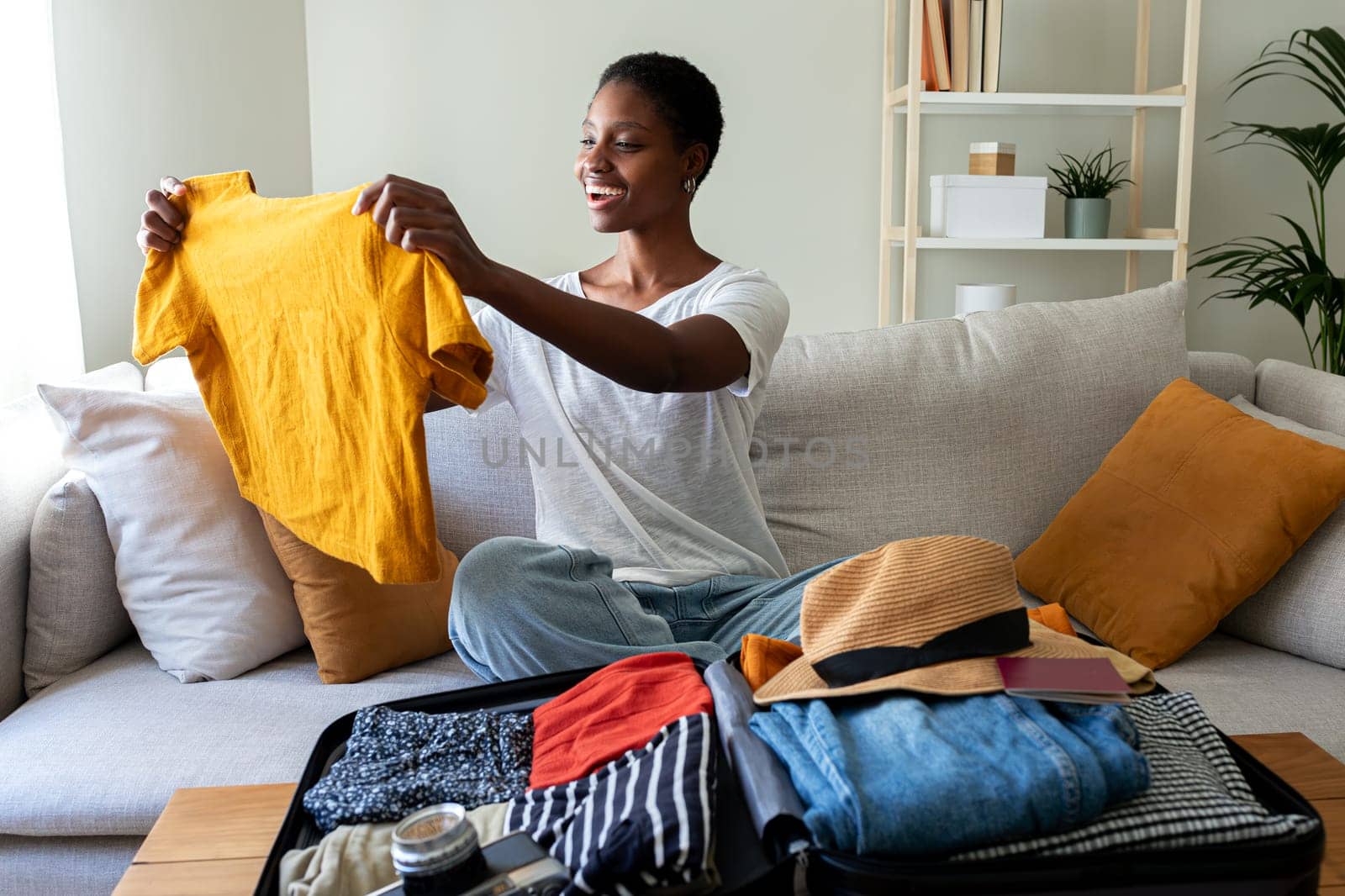 African American young woman folding t-shirt, packing suitcase for summer holiday trip. by Hoverstock