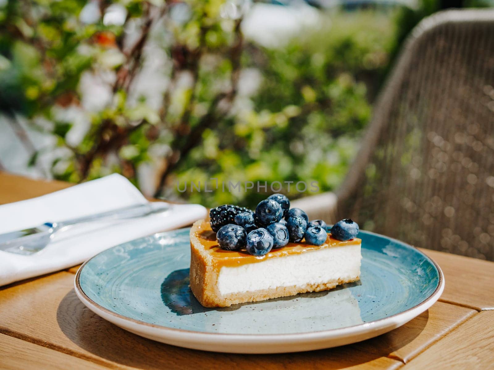 Piece of appetizing cheesecake or berry tart in blue rustic plate on wooden table outdoor in summer sunny day. New york cheesecake lifestyle shot