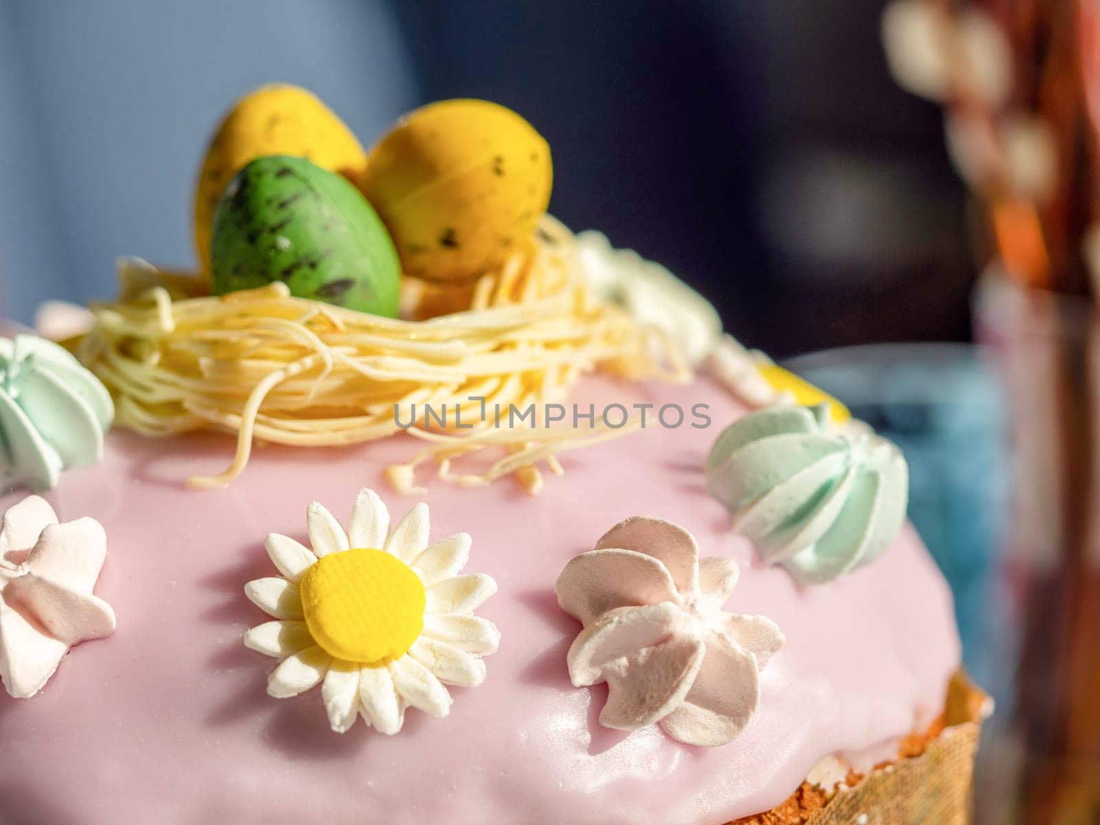 Delicious Easter cake with sugar glaze decorated chocolate eggs and merengue, close up. Festive orthodox easter cake kulich on the table and willow on background