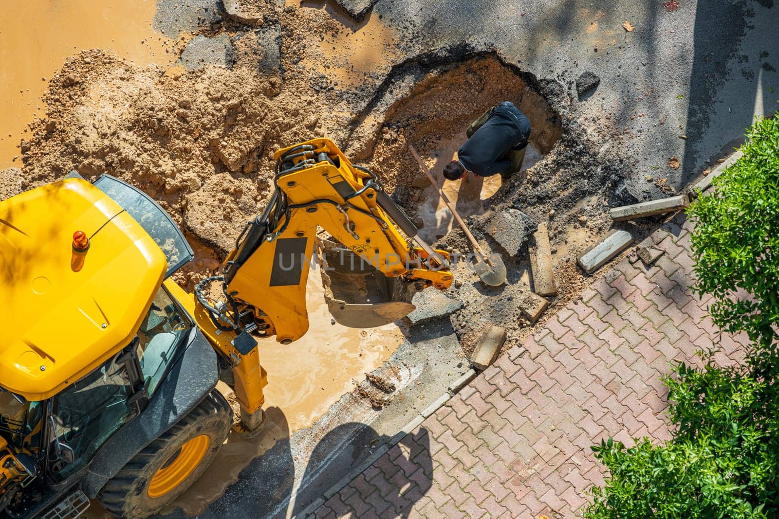 Digger digging asphalt to repair a water fault in a street by Sonat