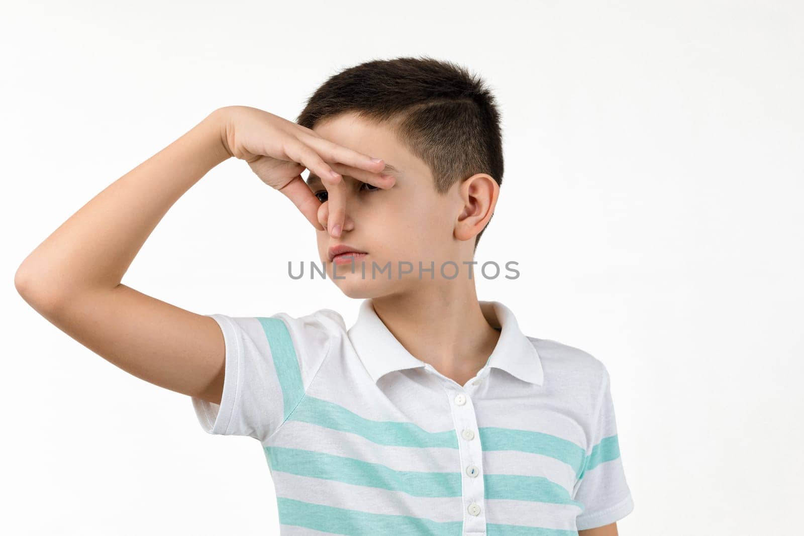 little child boy in striped t-shirt doing gesture smells bad on white background. facial expression. kid covers nose with hand, smells something awful