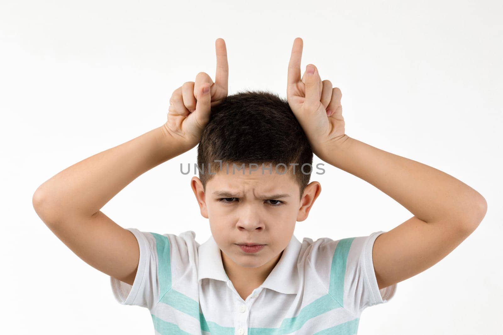 happy funny little child boy in striped t-shirt doing funny gesture with finger over head as bull horns on white background. facial expression