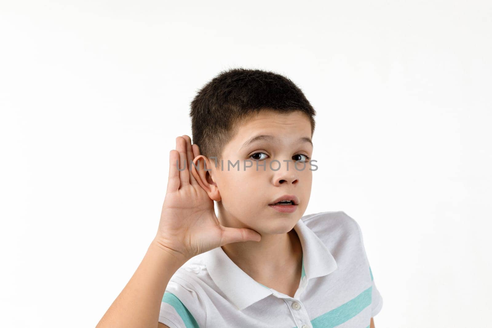 happy little child boy in striped t-shirt making hearing gesture on white background. facial expression. kid with hand over ear listening gossip.