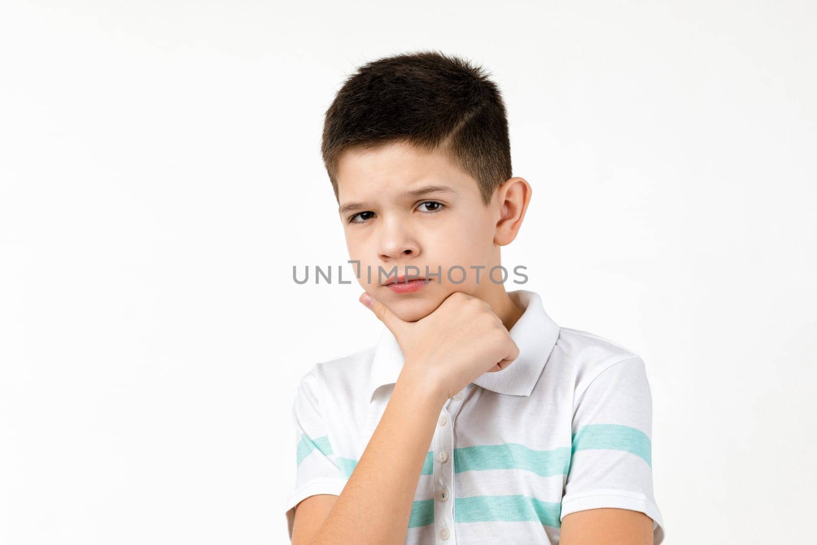 Cute little child boy in striped t-shirt thinks about something on white background. Human emotions and facial expression